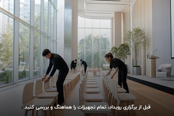 افرادی با لباس‌های مشکی در حال مرتب کردن صندلی‌ها تجهیزات در فضای برگزاری رویداد
